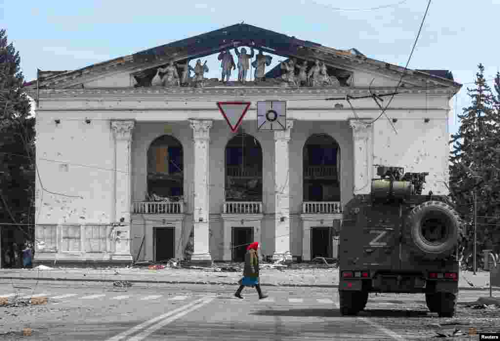 An elderly woman walks past the destroyed theater and an armored vehicle of pro-Russian forces in April 2022.&nbsp;