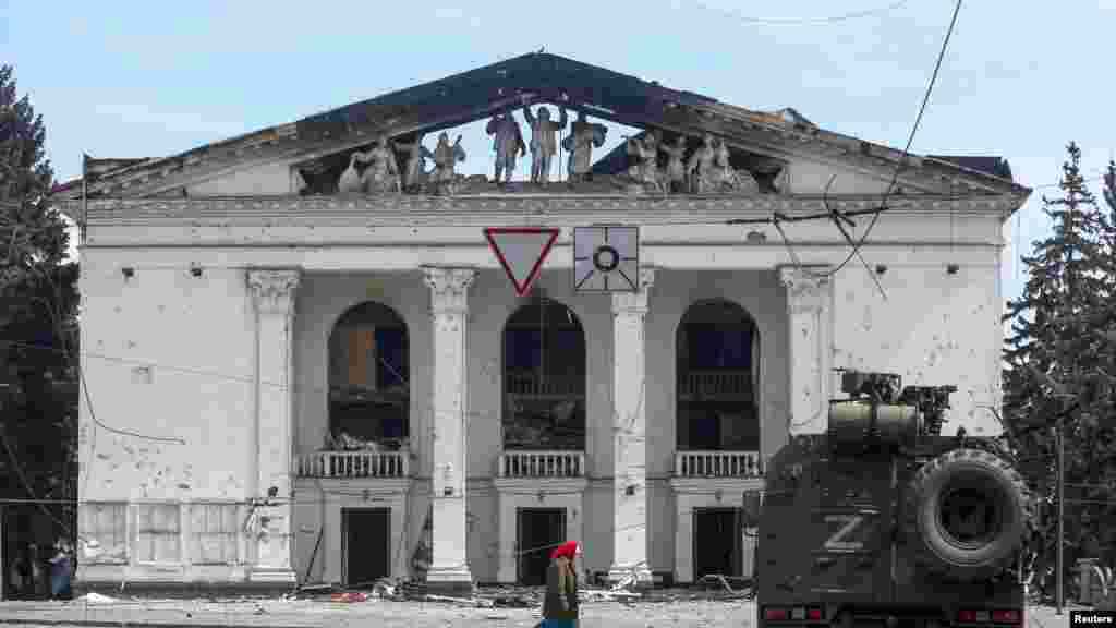 An elderly woman walks past the destroyed theater and an armored vehicle of pro-Russian forces in April 2022.&nbsp;