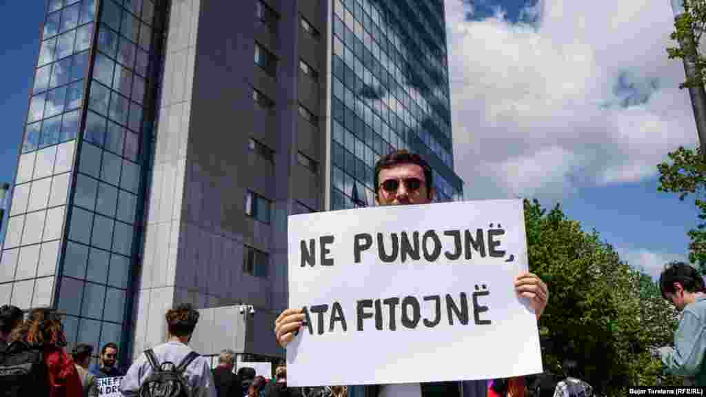 &quot;Ne punojmë ata fitojnë&quot; shkruan në panon e këtij protestuesi që protestoi para ndërtesës së Qeverisë së Kosovës më 1 maj 2022.