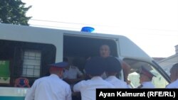 Полицейские заталкивают задержанного рядом с площадью человека в служебный микроавтобус. Алматы, 6 июля 2018 года.