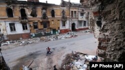 Дети идут среди разрушенных зданий в оккупированном Россией Мариуполе, 25 мая 2022 года