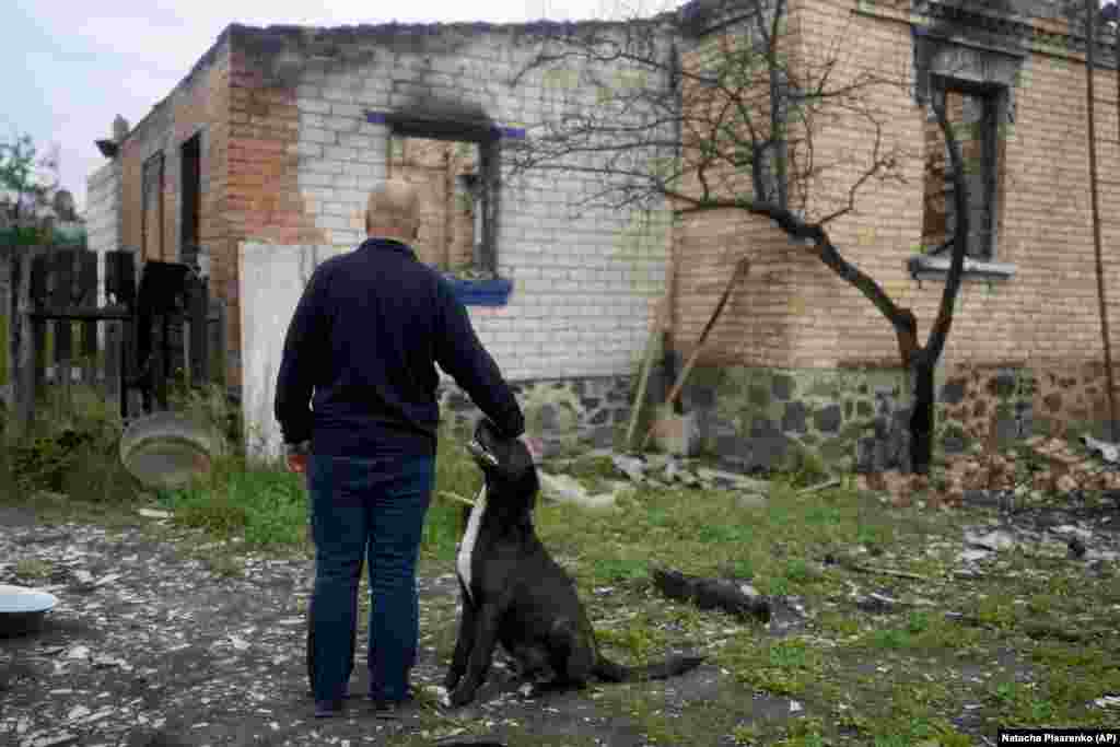 Eduard Zelenskiy looks at the ruins of his destroyed home while petting his dog.