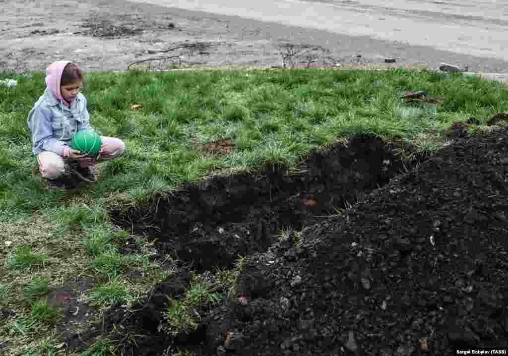 Девочка рядом с могилой, выкопанной у дороги во время осады Мариуполя, апрель 2022 года. Тела похороненных в парках Мариуполя выкапывают и перезахоранивают на Старокрымском кладбище
