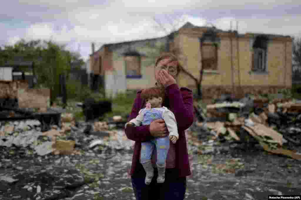 Nila Zelinska cries as she stands in the ruins of her home, holding a doll that belonged to her granddaughter.