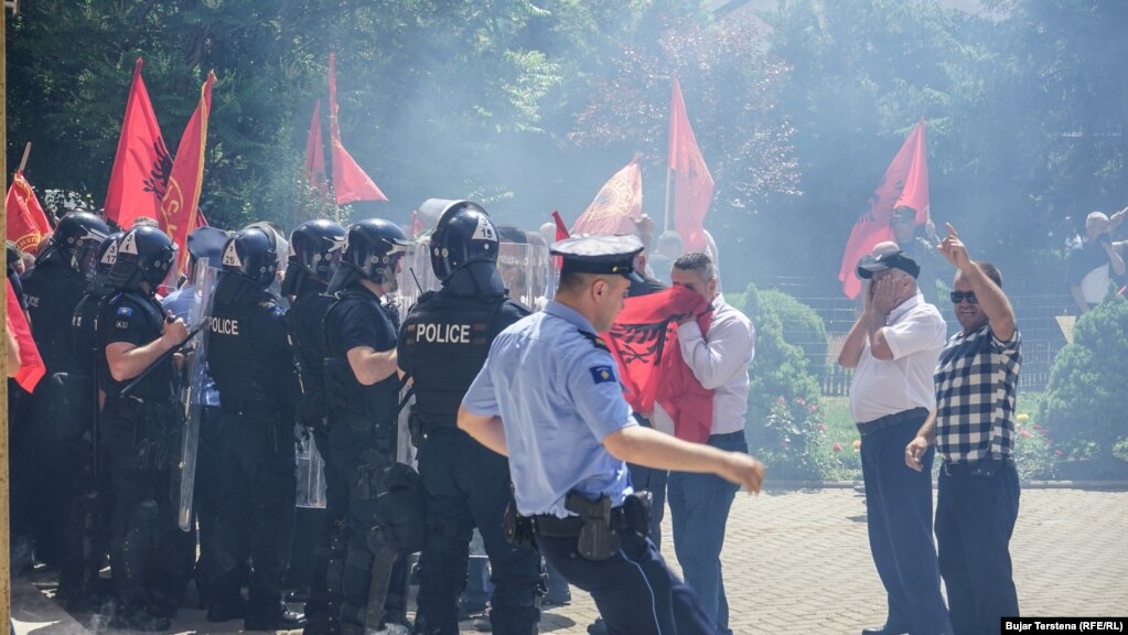 Një polic reagon derisa protestuesit mbulojnë fytyrën shkaku i gazit lotsjellës.&nbsp;Policia e Kosovës ka thënë nëpërmjet një deklarate se nuk ka përdorur gaz lotsjellës ndaj protestuesve.