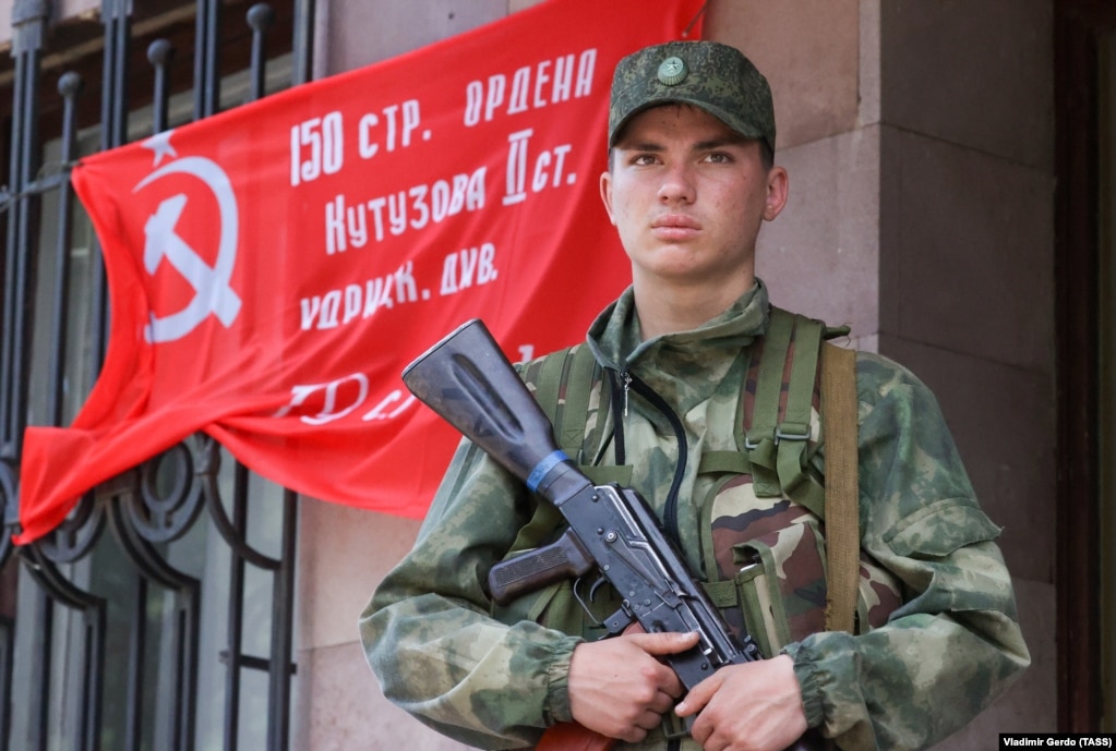 Një luftëtar pro-rus qëndron përpara një flamuri të epokës komuniste që u përdor për të shënuar fitoret sovjetike mbi Gjermaninë naziste në Luftën e Dytë Botërore. Fotografia është bërë në qytetin lindor të Ukrainës, Svitlodarsk, më 28 maj.