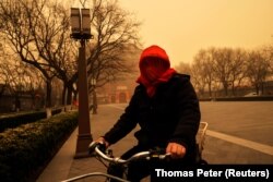 Žena sa prekrivenom glavom vozi bicikl u Pekingu pogođenim pješčanom olujom, 15. mart 2021.