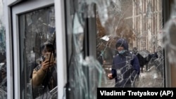 Мужчина фотографирует разбитые окна пункта полиции после протеста в Алматы 