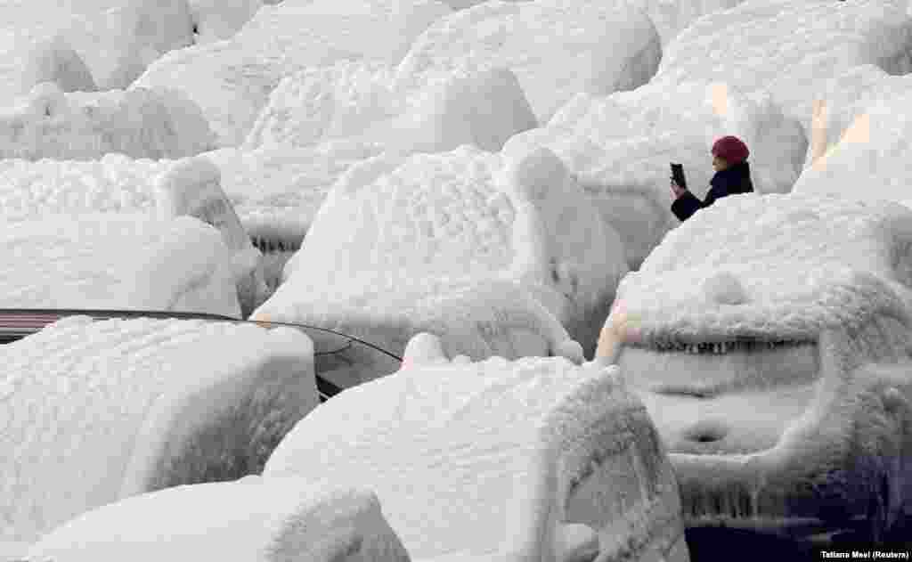 O femeie face o poză cu vehicule acoperite cu gheață descărcate de pe nava de marfă Sun Rio, în portul Vladivostok din Rusia. Nava a fost surprinsă de condiții meteorologice severe în Marea Japoniei.