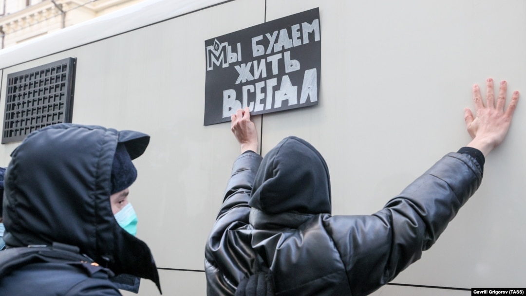A police officer detains a supporter of the Memorial society, which Russia has deemed a foreign agent, outside the Moscow Supreme Court in December 2021. The supporter holds a sign reading, "We will live always."