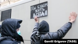 A police officer detains a supporter of the Memorial society, which Russia has deemed a foreign agent, outside the Moscow Supreme Court in December 2021. The supporter holds a sign reading, "We will live always."