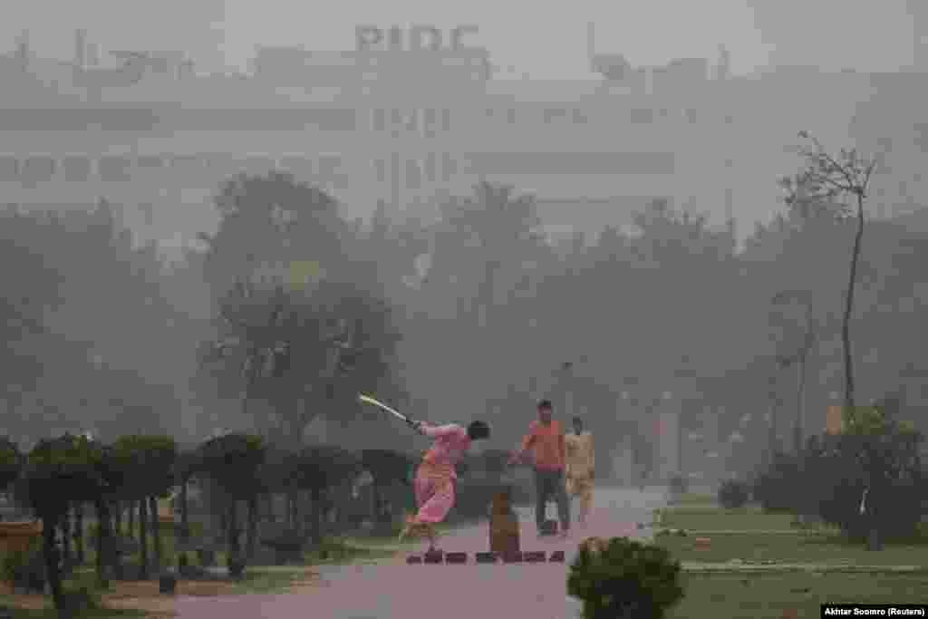 Boys play cricket in the rain at a park in Karachi, Pakistan.