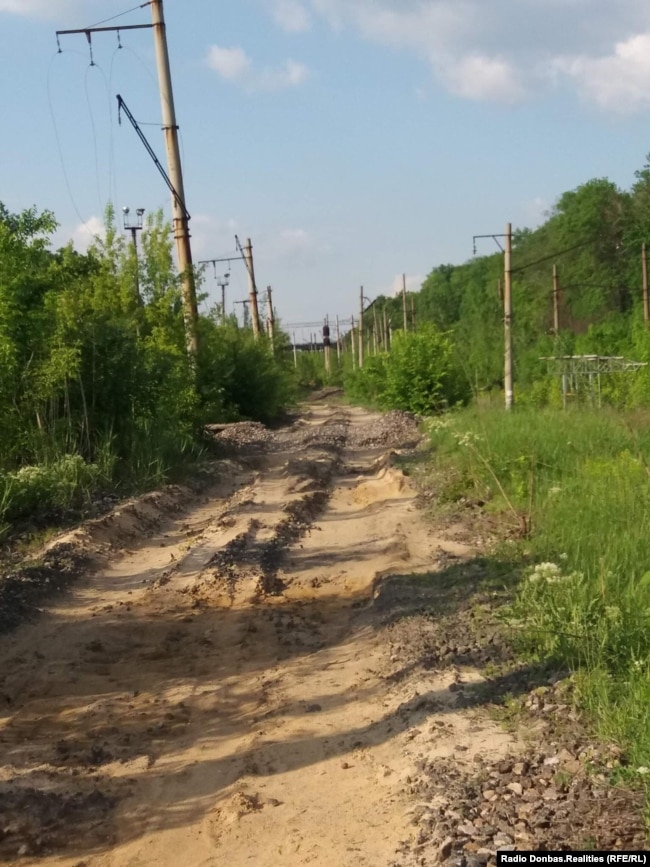 Видно, як насипана дорога перерізає недіючі залізничні колії. На задньому плані зруйнований Путилівський міст. Травень 2021 року