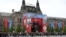 Members of a military band stand next to a screen broadcasting Russia's President Vladimir Putin's address during the Victory Day military parade in Moscow on May 9, 2026.