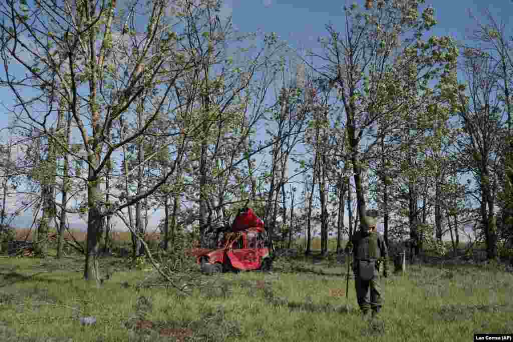 Украински војник ја проверува областа од неексплодирани убојни средства во близина на уништено цивилно возило