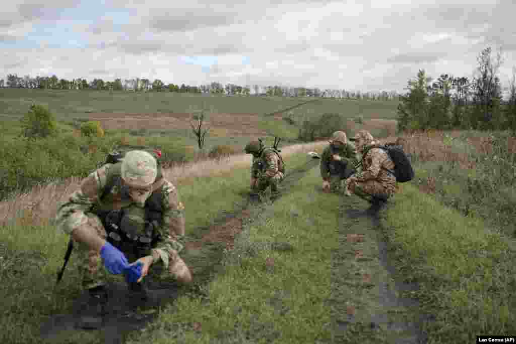 The recovery team crouches and waits as a deminer checks the body of a Ukrainian soldier for booby traps.