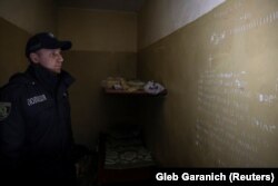 Un polițist ucrainean citește despre numărul de zile și o rugăciune care sunt mâzgălite pe peretele din subsolul unui birou de poliție, folosit de militarii ruși ca loc de detenție, în orașul Balakliia, recent eliberat de forțele armate ucrainene, în regiunea Harkov, Ucraina, 13 septembrie 2022.