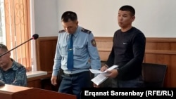 Ержан Елшибаев соттук отурумда милиция кызматкеринин кайтаруусунда. 