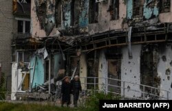 Un cuplu trece pe lângă o clădire avariată în Izium, regiunea Harkov, în estul Ucrainei, pe 11 septembrie 2022.