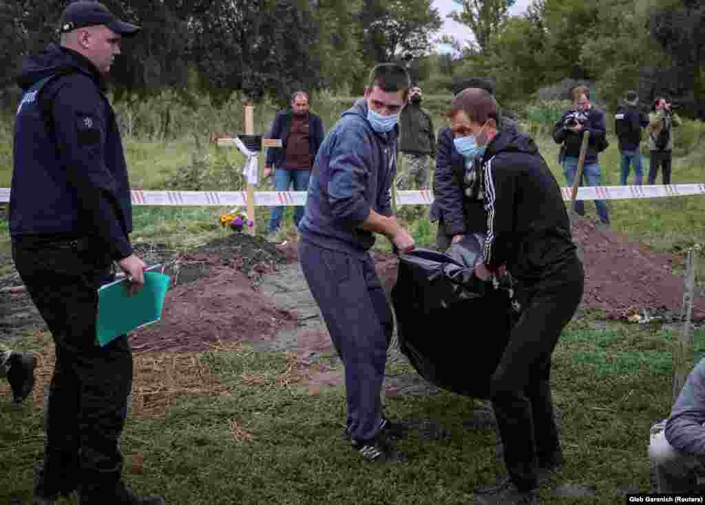 A police officer looks on as men carry the body of a person who, according to Ukrainian police, was killed by Russian troops in Balaklia.&nbsp;