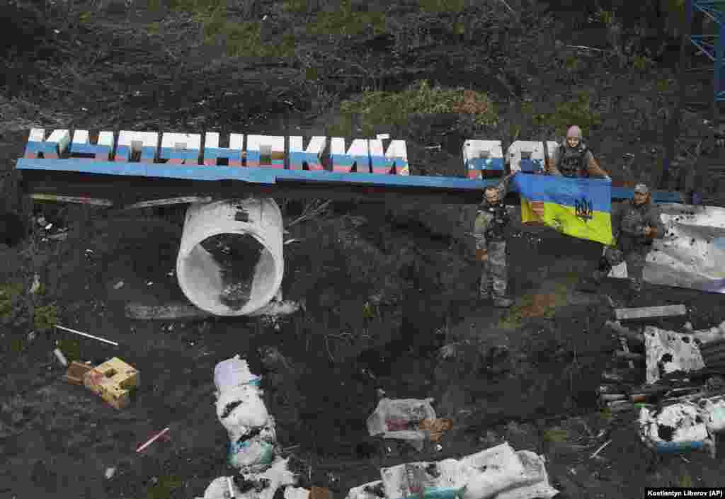 Ukrainian soldiers proudly show their national flag near the damaged &quot;Kupyansk district&quot; sign in the Kharkiv region.
