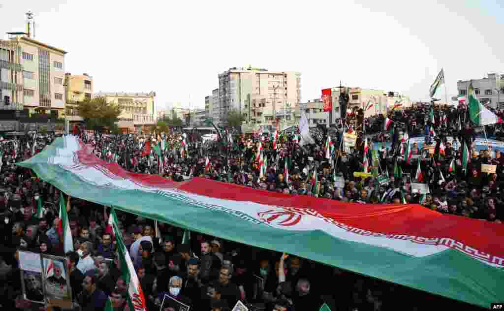 Iráni kormánypárti tüntetők feszítik ki nemzeti zászlajukat a közelmúltbeli kormányellenes tüntetésekkel szembeni tiltakozásul Teheránban 2022. szeptember 25-én