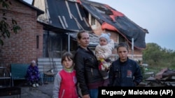 A 29 éves Margarita Tkacsenko gyermekeivel lerombolt házuk előtt a nemrég visszafoglalt Izjumban, Ukrajnában 2022. szeptember 25-én