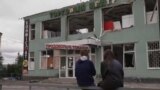 Two teenagers are sitting in front of a damaged building in Balaklya