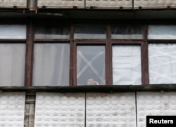 Жительница Горловки стоит перед окном, заклеенным скотчем, который защищает стекло в случае обстрелов
