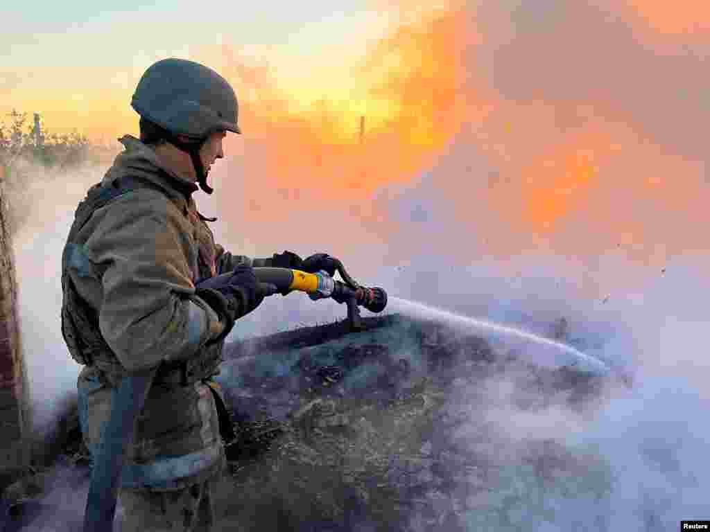 Egy ukrán tűzoltó próbál eloltani egy lángoló lakóépületet, amely egy orosz támadás során kigyulladt 2022. szeptember 5-én Bahmutban