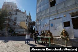 Женщины в ожидании голосующих во время незаконного организованного Россией референдума в Мариуполе на фоне разрушенных обстрелами зданий, 25 сентября