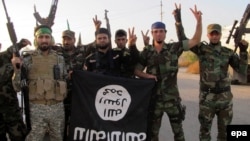 Members of the Hizbullah Brigades flash the victory sign while holding an Islamic State group flag in southern Iraq in October 2014.