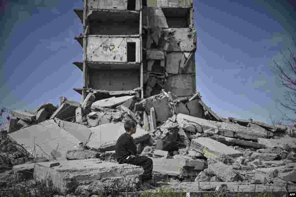 Egy&nbsp;kisfiú&nbsp;egy lerombolt lakóház előtt üldögél a kelet-ukrajnai Kramatorszkban
