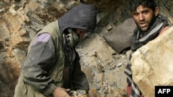 Afghan miners drill into rock in a makeshift emerald mine.