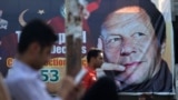 PAKISTAN -- Pakistani men sit near a poster of Pakistan's cricketer-turned politician and head of the Pakistan Tehreek-e-Insaf (Movement for Justice) party Imran Khan, in Islamabad, July 30, 2018