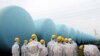 Japan Nuclear Regulation Authority (NRA) employees with protective suits and masks inspect makeshift tanks storing contaminated water at the TEPCO Fukushima Daiichi nuclear power plant.