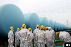 Сотрудники комиссии по ядерному регулированию Японии в защитных костюмах инспектируют место хранения цистер с зараженной водой на территории АЭС "Фукусима". 23 августа 2013 года.