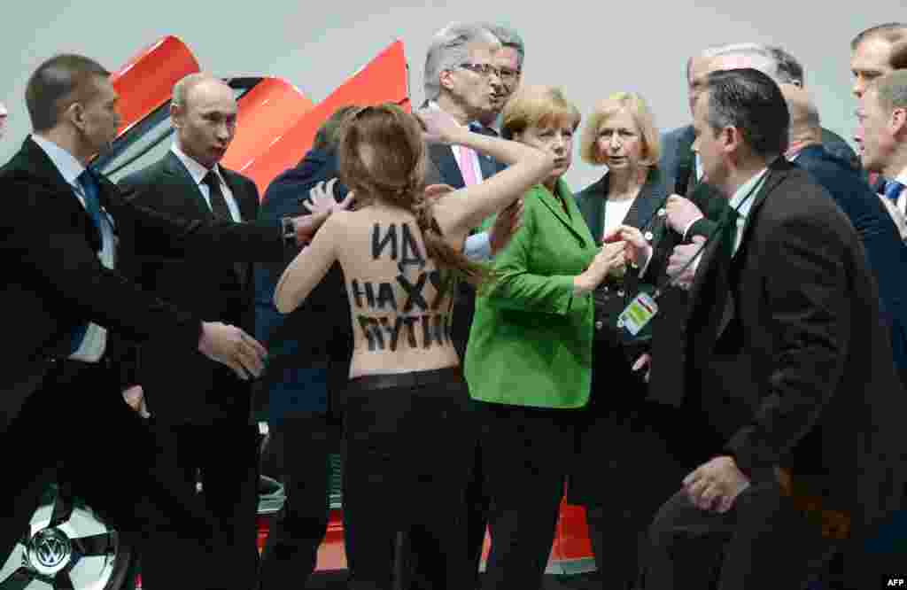 A topless demonstrator with an obscene message written on her back walks toward Russian President Vladimir Putin (left) and German Chancellor Angela Merkel during their visit to the Hanover Industrial Fair. Four demonstrators from the Femen group protested against Putin as he was visiting the Volkswagen stand. (AFP/Jochen L&uuml;bke)