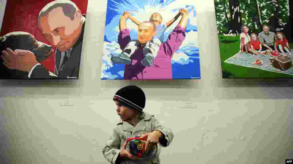 A boy stands in front of the paintings by artist Aleksei Sergiyenko at his exhibition &quot;President. The Kindest Person,&quot; marking the 60th birthday of President Vladimir Putin at the Flacon design workshop in Moscow. (AFP/Andrei Smirnov)