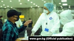 Медики в защитных костюмах и пассажир в бишкекском аэропорту Манас. 18 марта 2020 года.