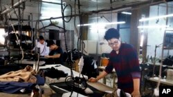 In this July 26, 2018 photo, Afghan musician Mohammad Rezai, right, a member of the Arikayn rock band, works as a tailor in Pakdasht, on the outskirts of Tehran, Iran. The four rockers that make up the band, known as Arikayn, that plays Metallica-inspired