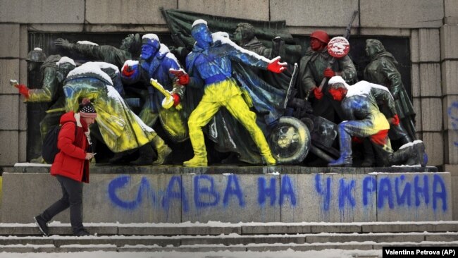 Një burrë duke ecur pranë një monumenti të ushtrisë sovjetike të ngjyrosur me ngjyrat e flamurit ukrainas, kurse poshte shkruan "Lavdia e Ukrainës", Sofje. Fotografi e bërë më 28 shkurt 2022.
