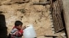 A Pakistani boy drinks water from a gallon container outside his makeshift tent in an Islamabad slum.