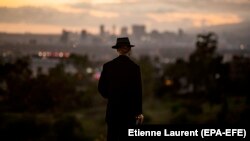 Американец с бутылкой вина на холме в центре Лос-Анджелеса наблюдает закат солнца в дни эпидемии. 23 марта 2020 года