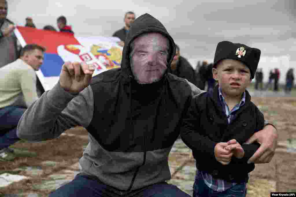 A Serb with a child wears a face mask depicting Serbian war criminal Ratko Mladic as he participates in a ceremony commemorating a medieval battle with invading Ottoman forces in 1389 at Gazimestan, Kosovo. Hundreds of Serbs gathered to mark the 629th anniversary of the battle in which a Serbian army was defeated by the Ottoman Empire. (AP/Visar Kryeziu)