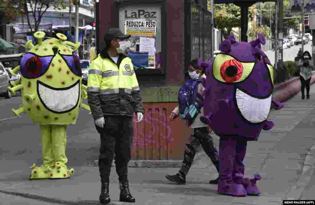 A Bolivian police officer in La Paz on duty next to two people in coronavirus costumes. Bolivia&#39;s interim president, Jeanine Anez, announced a national quarantine on March 23.
