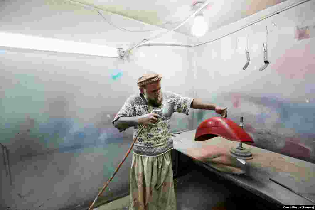 A worker sprays a restored mudguard for a scooter at a Vespa restoration and repair workshop in Islamabad.