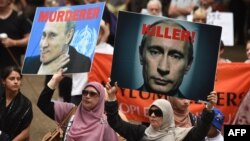Демонстранты держат фотографии президента России Владимира Путина в знак протеста против участия России в сирийской гражданской войне, а также поддержку беженцев, ищущих убежище в Австралии. Сидней, 11 октября 2015 года.