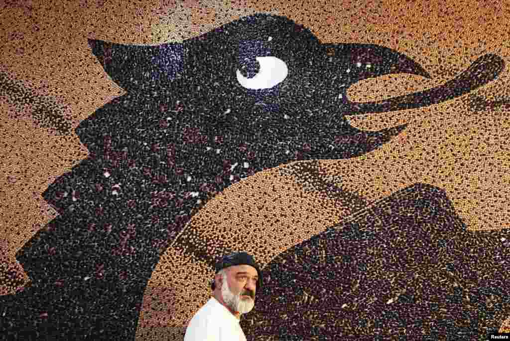 Albanian artist Saimir Strati appears in front of his mosaic of the Albanian flag at the Hotel Prishtina. The 65-square-meter mosaic, made of 1.35 million beans, earned Strati his seventh Guinness world record.