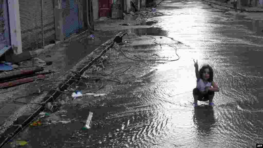 A girl flashes the sign for victory in a destroyed street flooded with water in the restive central Syrian city of Homs. (Reuters/Shaam News Network)